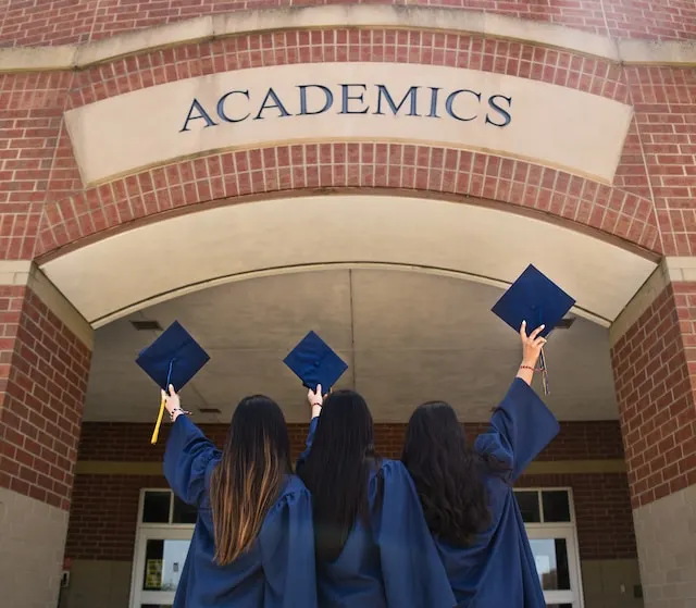 kobi education-daftar kampus lpdp luar negeri-gambar logo academics di depan kampus dengan tiga wisudawan sambil mengangkat topi toga mereka dengan gembira