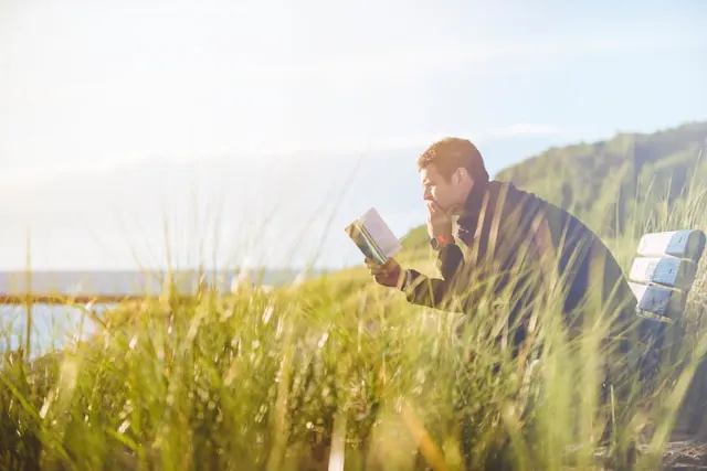 kobi education-jurusan luar negeri-gambar pria sedang membaca buku di tengah ladang