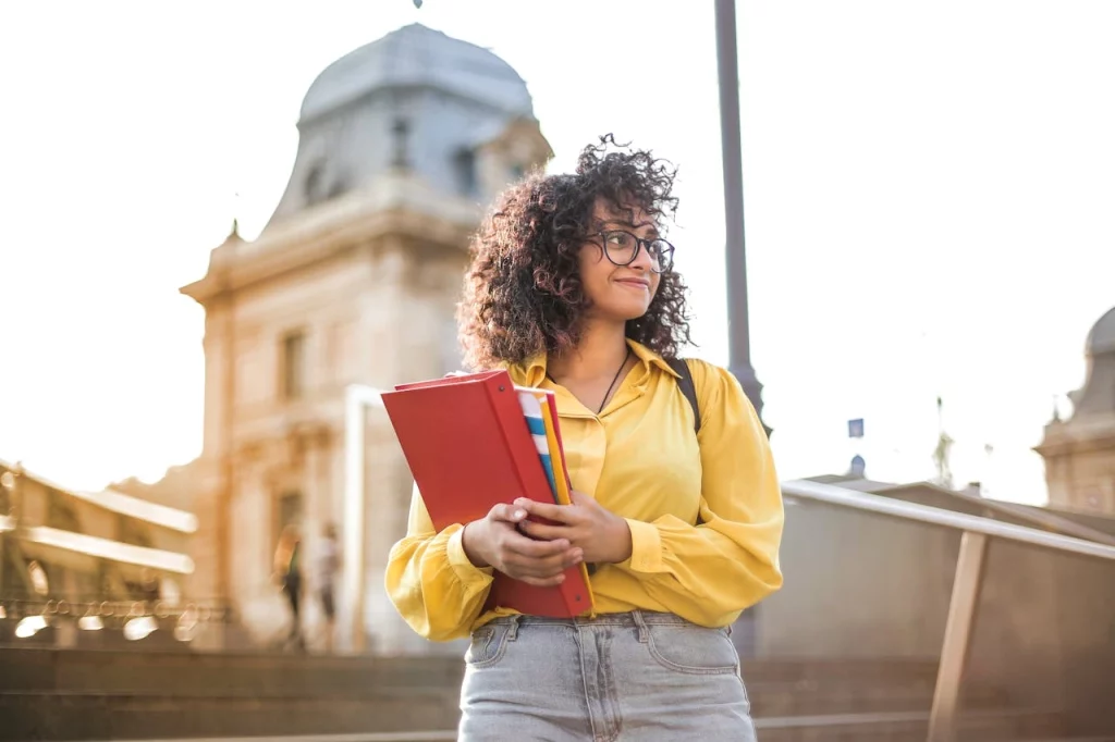 kobi education-cara studi ke luar negeri-gambar perempuan yang memakai baju kuning sedang membawa peralatan untuk belajar