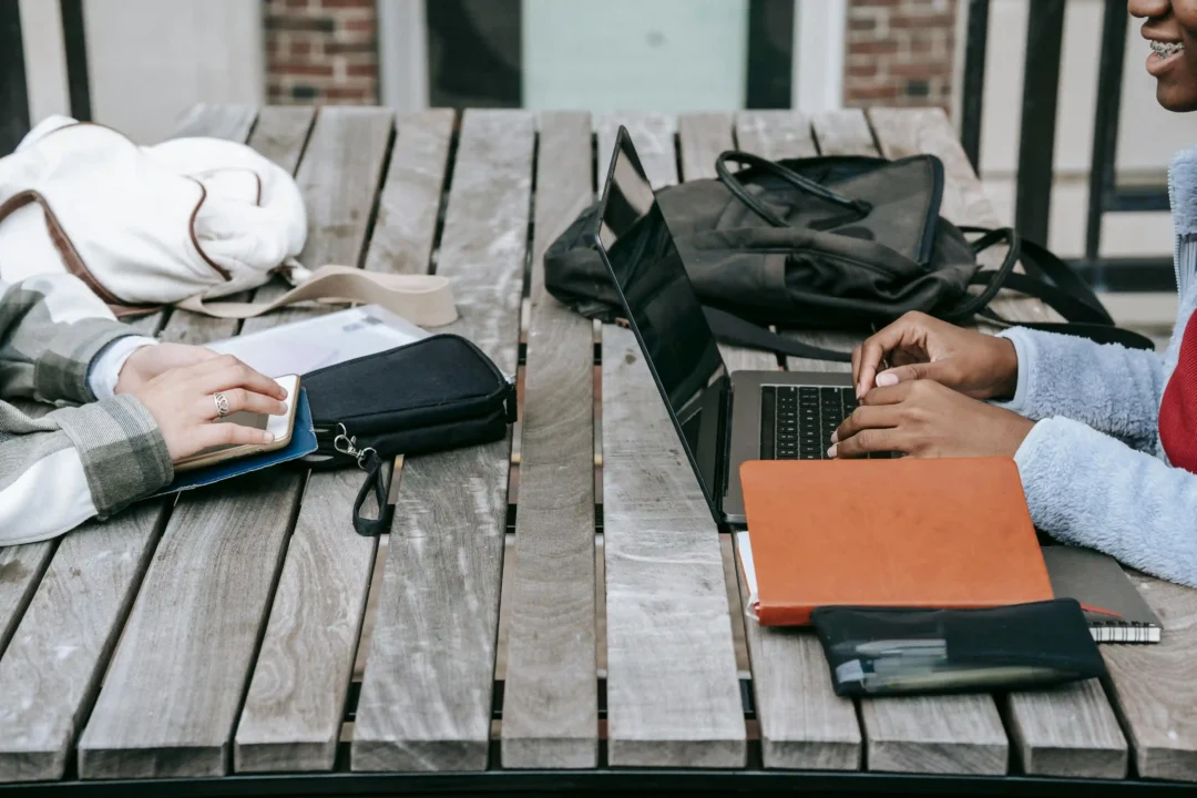 kobi education-berkas beasiswa rotary yoneyama-gambar dua mahasiswa sedang mempersiapkan berkas secara online melalui laptop mereka di meja taman