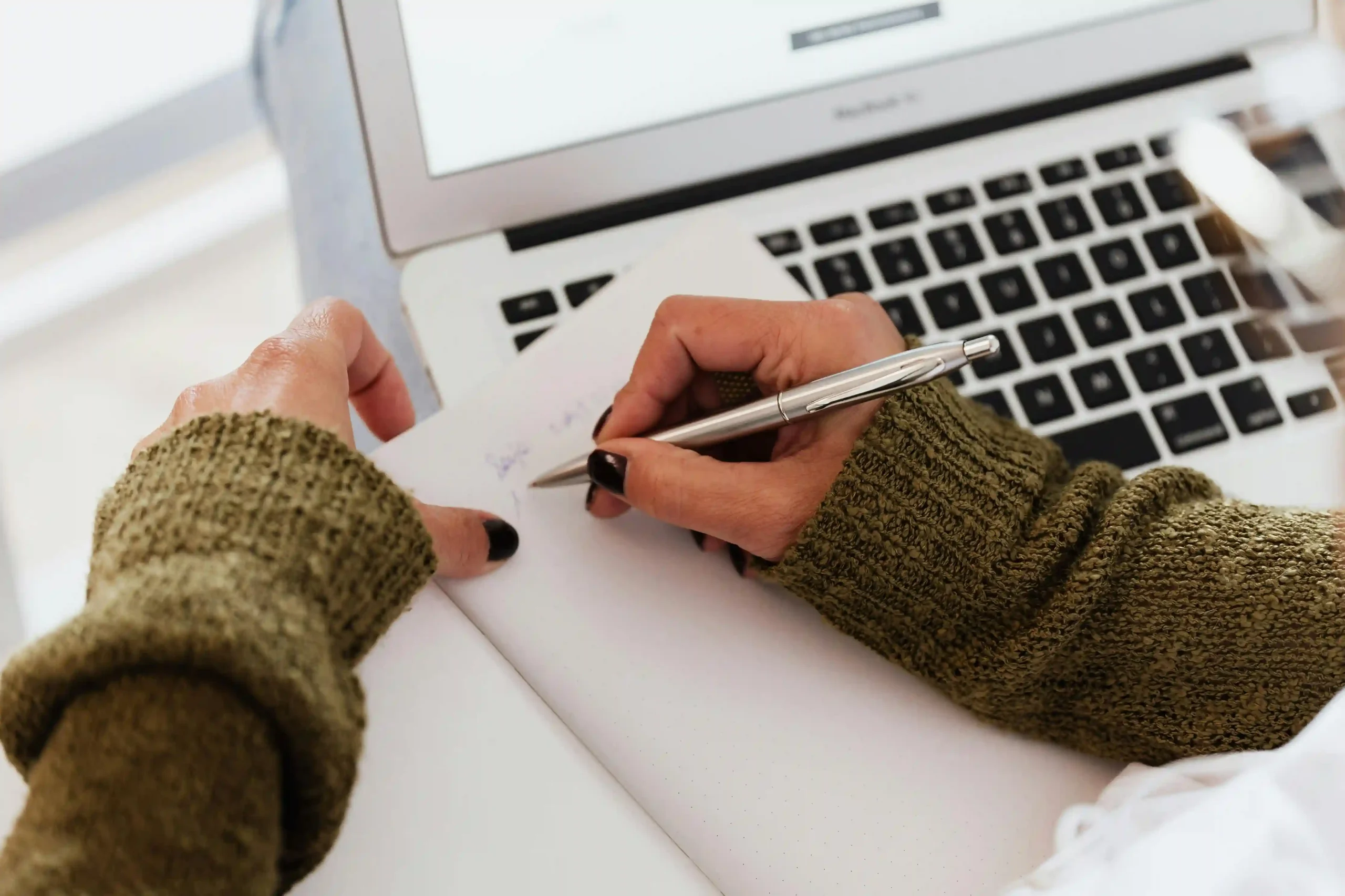 kobi education-universitas yang menerima toefl ibt buat s2-gambar tangan seseorang sedang mencatat di jurnal yang terletak di atas laptop mereka
