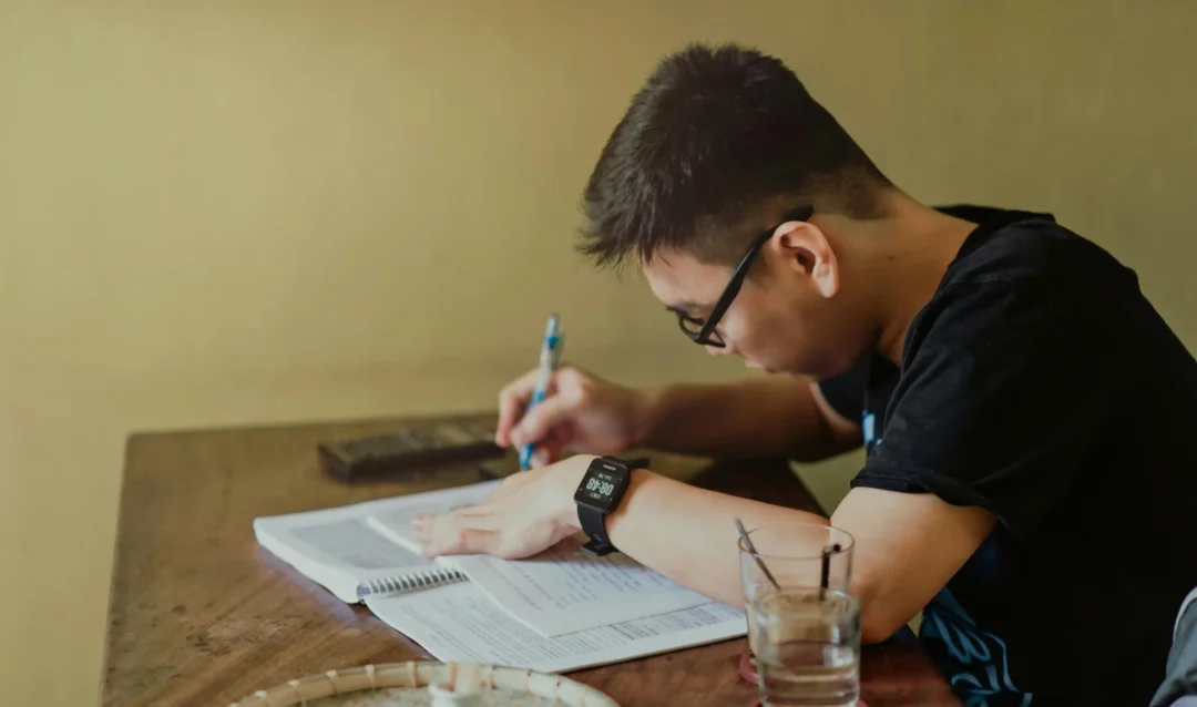 kobi education-beasiswa parsial malaysia-gambar pria sedang mengerjakan soal dengan sendirian di ruangan yang memiliki dinding berwarna kuning tua